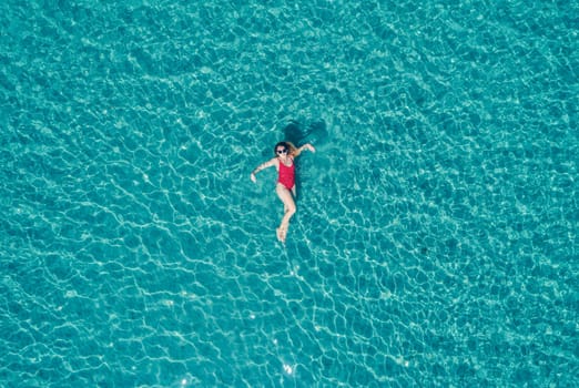 Aerial View of a Woman in Red Swimsuit Floating Serenely on the Crystal Clear Ocean Waters During Midday