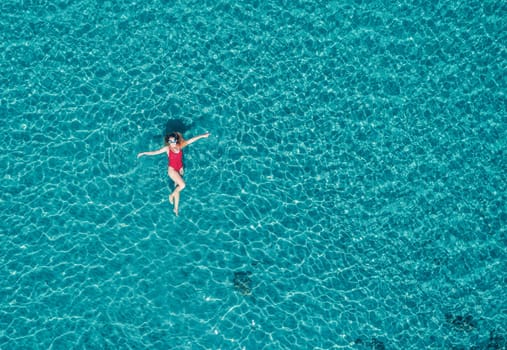 Aerial View of a Woman in Red Swimsuit Floating Serenely on the Crystal Clear Ocean Waters During Midday