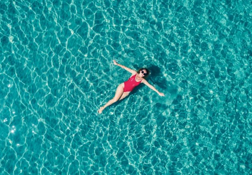 Aerial View of a Woman in Red Swimsuit Floating Serenely on the Crystal Clear Ocean Waters During Midday