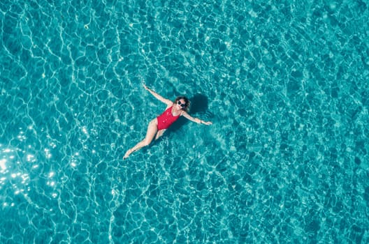 Aerial View of a Woman in Red Swimsuit Floating Serenely on the Crystal Clear Ocean Waters During Midday