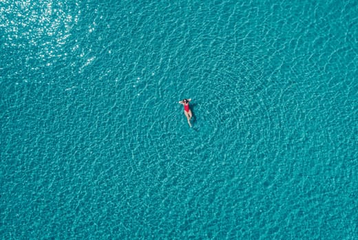 Aerial View of a Woman in Red Swimsuit Floating Serenely on the Crystal Clear Ocean Waters During Midday