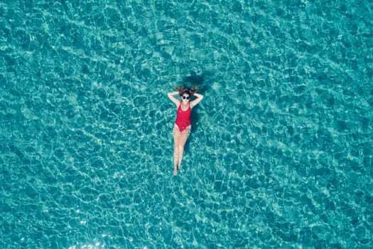 Aerial View of a Woman in Red Swimsuit Floating Serenely on the Crystal Clear Ocean Waters During Midday