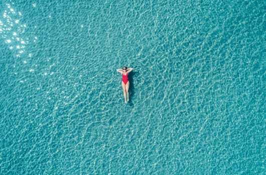 Aerial View of a Woman in Red Swimsuit Floating Serenely on the Crystal Clear Ocean Waters During Midday