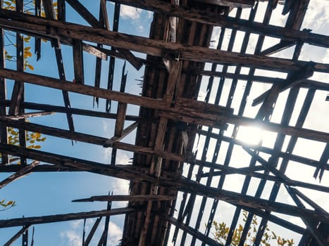 Bottom view of the roof of an old building with wooden structures against the sky. Destroyed wooden roof in the abandoned building.