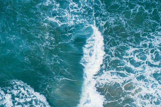 Aerial view of white foam on the surface of the blue sea.