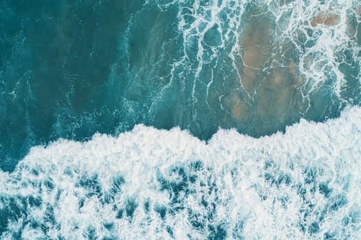 Aerial view of white foam on the surface of the blue sea.