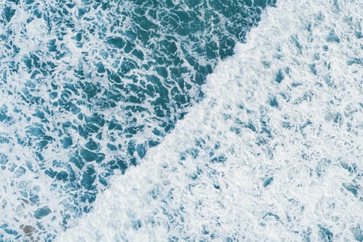 Aerial view of white foam on the surface of the blue sea.