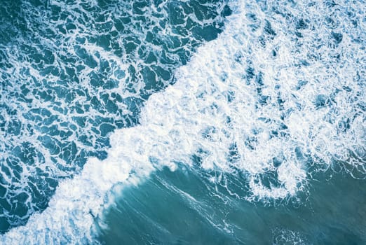 Aerial view of white foam on the surface of the blue sea.