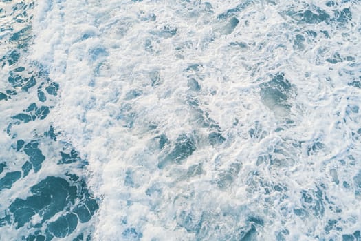 Aerial view of white foam on the surface of the blue sea.