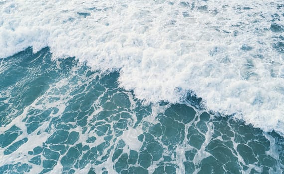 Aerial view of white foam on the surface of the blue sea.