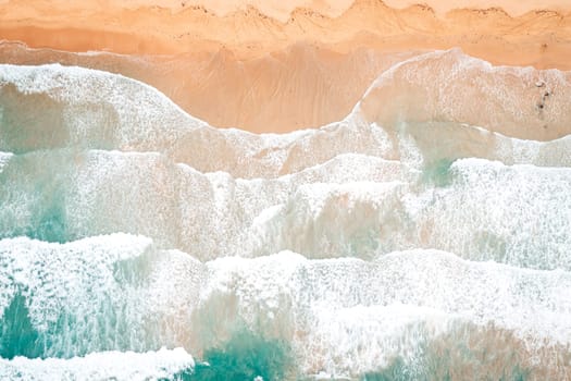 Aerial top view of turquoise ocean wave reaching the coastline.