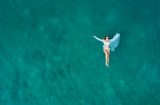 Top view of young pretty sexy girl in white swimsuit floating on water surface in crystal clear turquoise ocean.