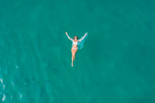 Top view of young pretty sexy girl in white swimsuit floating on water surface in crystal clear turquoise ocean.