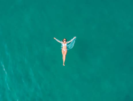 Top view of young pretty sexy girl in white swimsuit floating on water surface in crystal clear turquoise ocean.