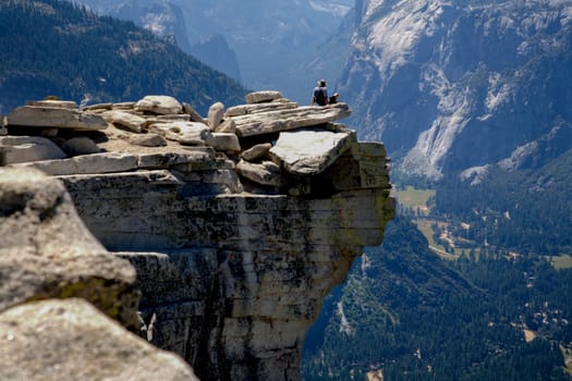 SOLO HIKER RELAXING ON HALF DOME IN YOSEMITE NATIONAL PARK, CALIFORNIA. THE VALLEY IS 4,000 FEET BELOW