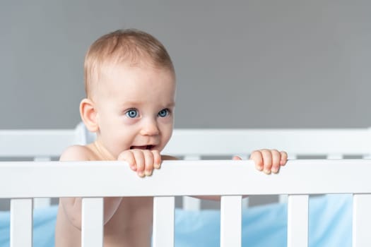 Baby with a sly expression on the face of a little prankster in a white classic crib.