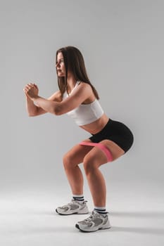 Caucasian woman doing squats with fitness band on white background. Vertical photo