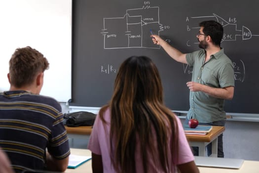 Male caucasian teacher pointing blackboard explaining new concepts to multiracial high school students. Education concept.