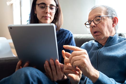 Senior man explaining to his young daughter with help of digital tablet. Family members sharing technology.