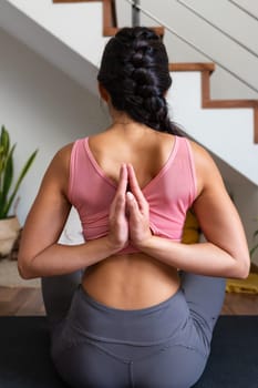 Rear view of young woman doing reverse prayer yoga pose at home living room. Female yogi doing namaste mudra behind back. Vertical image. Lifestyle and spirituality concept.