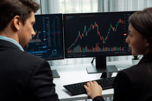 Two business traders discussing on dynamic stock market in currency rate investment trading on two pc screens with compare real time graph on risk or profit point of data at modern office. Postulate.