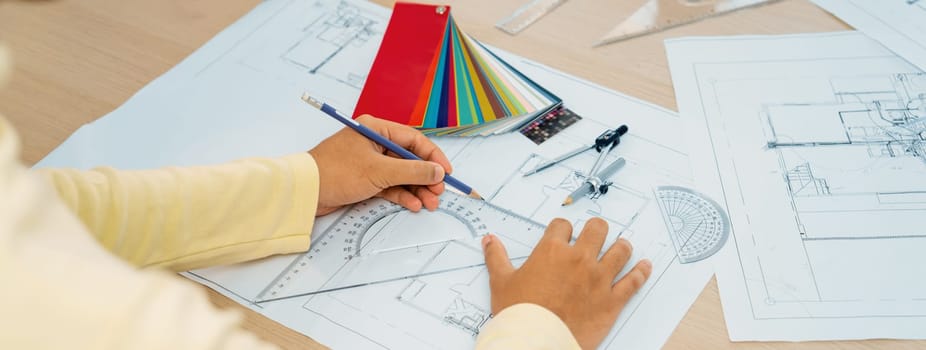 Cropped image of professional architect designer hand draws blueprint while project manager shows the mistake point with architectural document, color palette scatter around. Closeup. Variegated.