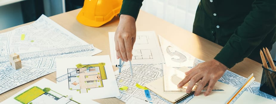 A portrait of architect using divider to measure blueprint. Architect designing house construction on a table at studio, with architectural equipment scattered around. Focus on hand. Delineation