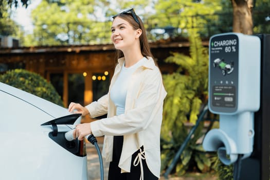 Young woman and sustainable urban commute with EV electric car recharging at outdoor cafe in springtime garden, green city sustainability and environmental friendly EV car. Expedient