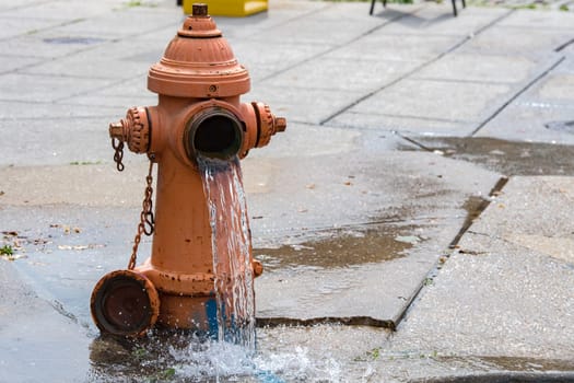 Street orange hydrant with water falling on the street in Baltimore, Usa