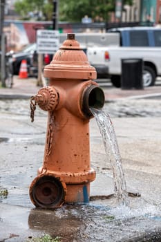 Street orange hydrant with water falling on the street in Baltimore, Usa