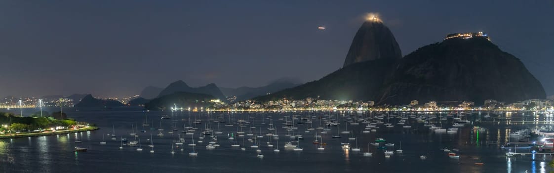 Stunning night panorama of Rio's bay with boats and Sugarloaf Mountain.