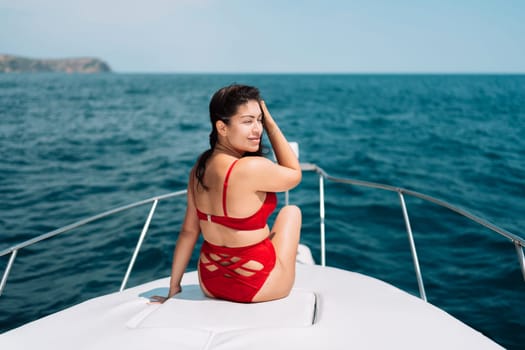 Yacht woman in a red bikini posing while on the bow of a yacht. Happy woman is sunbathing on the bow of a ship during a boat trip. Travel concept, vacation at sea.