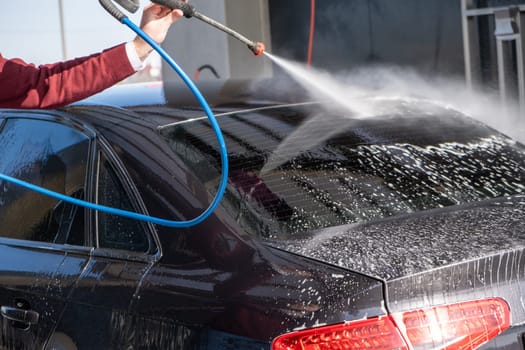 A man washes off the foam while washing the car. A vehicle is engulfed in soapy foam during a car wash, covering the tires, wheels, hood, and entire exterior of the car. Self-service car wash