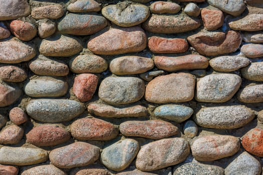 wall made of many colorful round stones under direct sun light, full-frame background and texture.