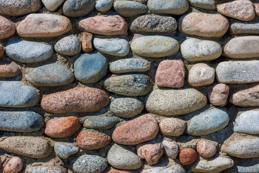 wall made of many colorful round stones under direct sun light, full-frame background and texture.