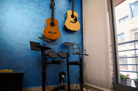 A modern interior of a music studio at home. Acoustic and electric guitars hanging on blue color wall and drum set. Hobbies and leisure. Musician's room for playing and learning music. Horizontal shot