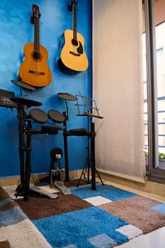 Modern interior of a music studio for home use. Acoustic nd electric guitars hanging on blue color wall and drum set. Hobbies and leisure. Musician's room for playing and learning music. Vertical shot