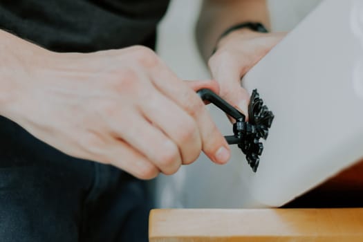 Hands of a young Caucasian unrecognizable man removes an antique carved black handle on a white drawer, close-up side view.