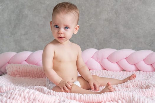 The baby sits on the bed and just looks at the camera. Universal photo.