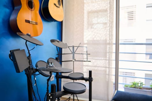 Modern interior of a music studio for teen musicians. Acoustic and electric guitars hanging on blue wall and drum kit with black cymbals. Musician's room for playing and learning music. Copy ad space