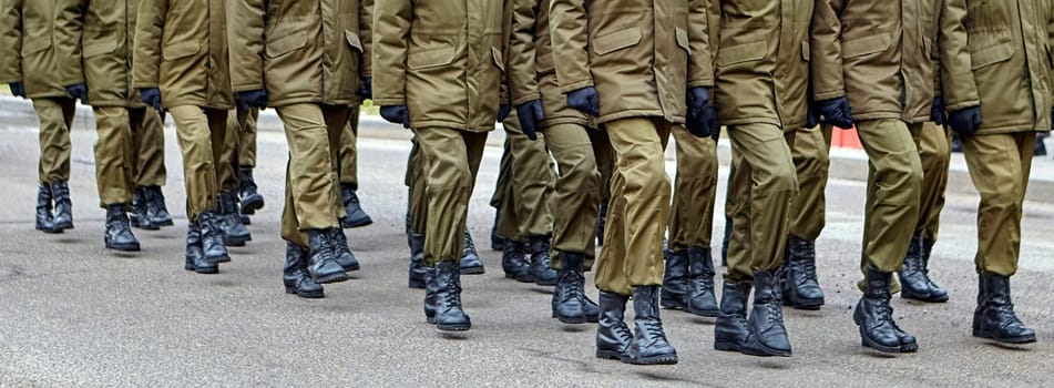 Army soldiers in uniform stand in formation on a concrete surface with yellow crosswalk lines. They wear combat fatigues and boots, showing discipline and readiness.