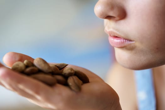 Closeup of crop unrecognizable teenage girl with handful of almonds at home