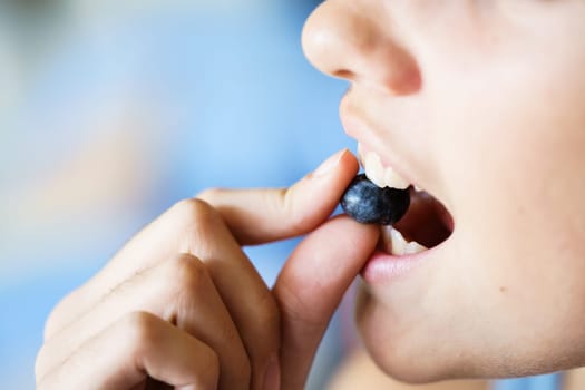 Closeup of crop anonymous young girl biting delicious organic blueberry at home