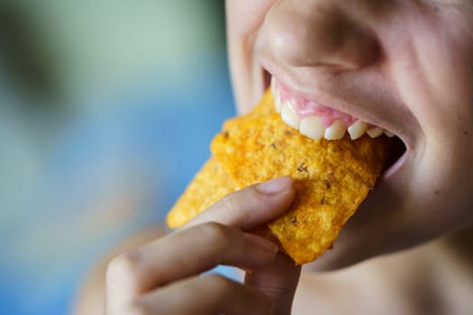 From above of crop unrecognizable teenage girl biting delicious Mexican tortilla chips at home