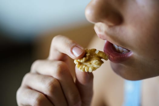 From above closeup of crop anonymous teenage girl eating healthy walnut kernel at home