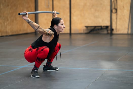 Side view photo with copy space of a mature woman squatting with a bar in a gym