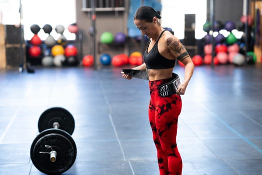 Mature sportive strong woman tying a belt to prevent injures while weightlifting