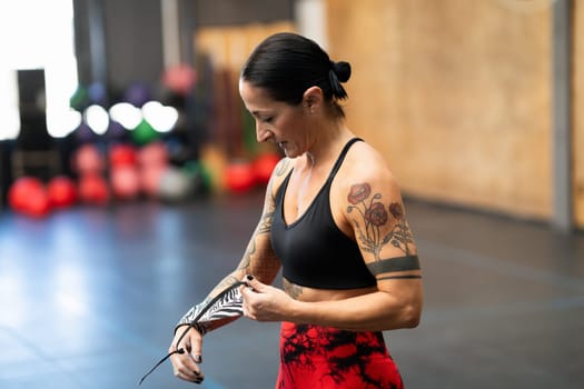 Strong mature woman protecting her wrists with wraps before training in a gym