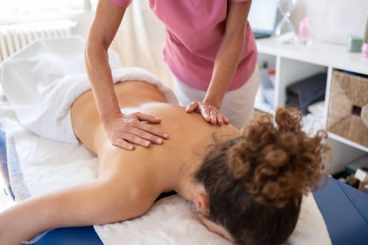 High angle of crop anonymous masseuse kneading back of woman during treatment in physical therapy clinic releasing muscle tension