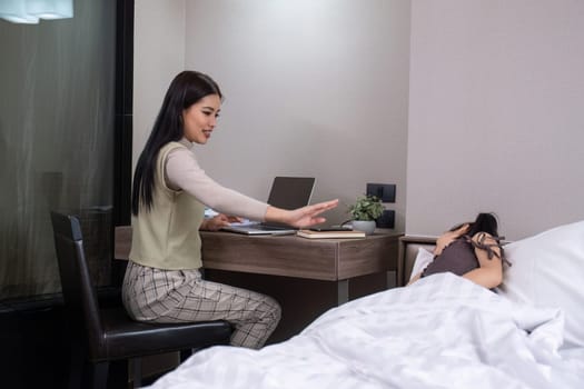 Young woman, single mother, with cute daughter in bedroom A young woman is working online on her laptop from home with her daughter waiting on her bed..